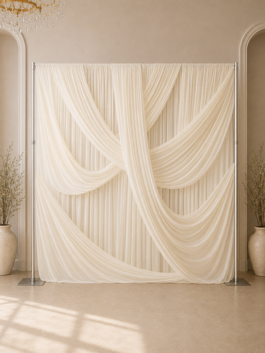A draped cream fabric backdrop on a metal stand, styled in an elegant indoor setting with beige walls, arched doorways, and potted plants.